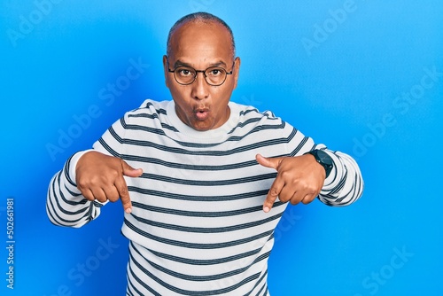 Middle age latin man wearing casual clothes and glasses pointing down with fingers showing advertisement, surprised face and open mouth