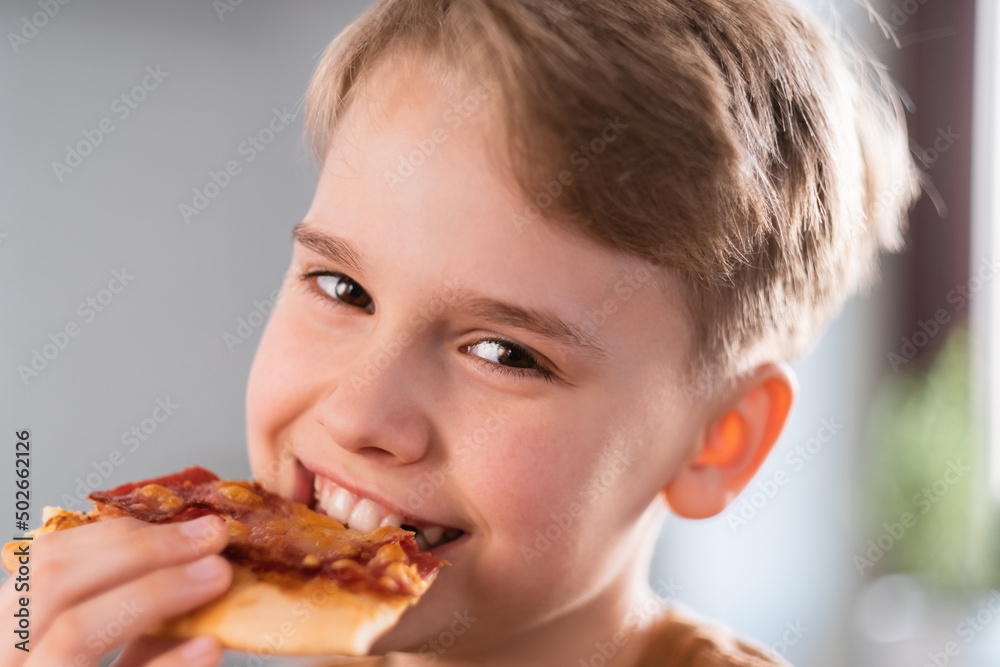 Happy teen boy enjoying eating delicious pizza at home. Portrait of a cute teenager Happy teen boy enjoying eating delicious pizza at home. Portrait of a cute teenager