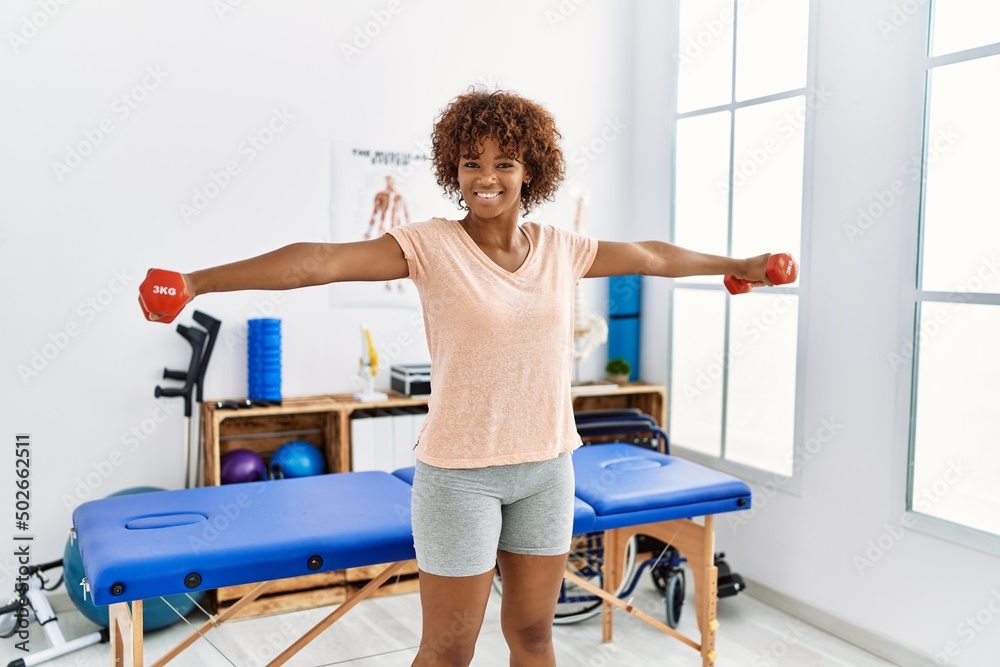Young african american woman doing rehab using dumbbells at clinic