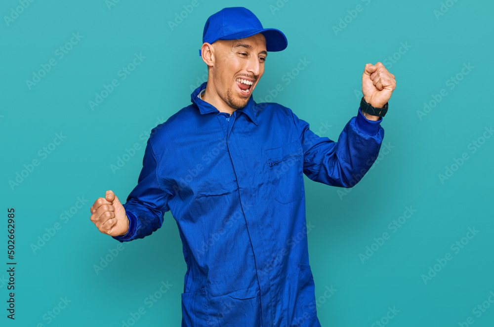 Bald man with beard wearing builder jumpsuit uniform dancing happy and cheerful, smiling moving casual and confident listening to music