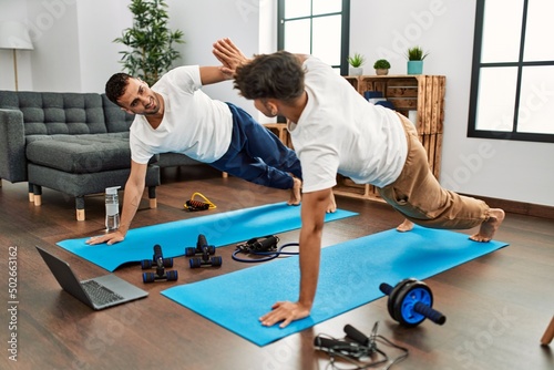 Two hispanic men couple smiling confident having online abs exercise class at home