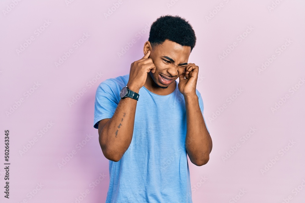Young african american man wearing casual blue t shirt covering ears with fingers with annoyed expression for the noise of loud music. deaf concept. Young african american man wearing casual blue t shirt covering ears with fingers with annoyed expression for the noise of loud music. deaf concept.