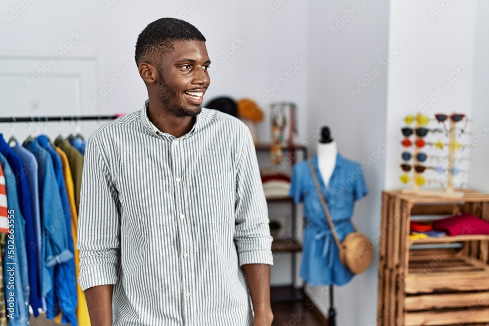 Fototapeta premium Young african american man working as manager at retail boutique looking away to side with smile on face, natural expression. laughing confident.