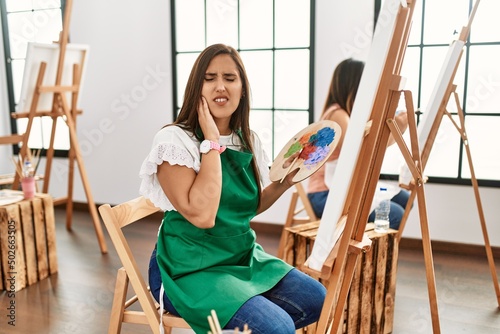 Young hispanic artist women painting on canvas at art studio touching mouth with hand with painful expression because of toothache or dental illness on teeth. dentist concept.