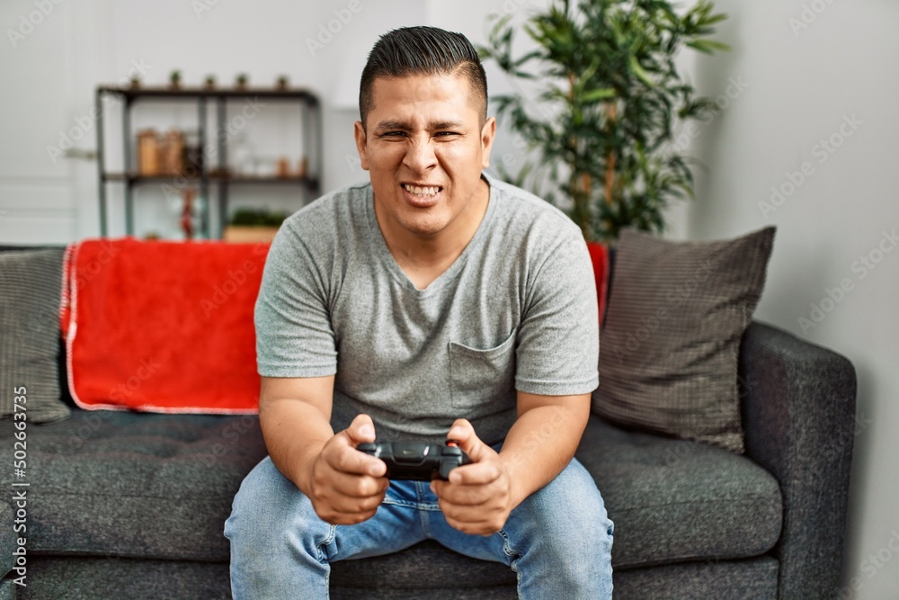 Young hispanic man angry playing video game at home. Young hispanic man angry playing video game at home.