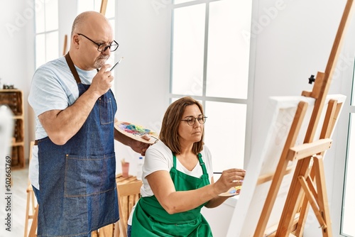 Middle age hispanic painter couple with serious expression painting at art studio.