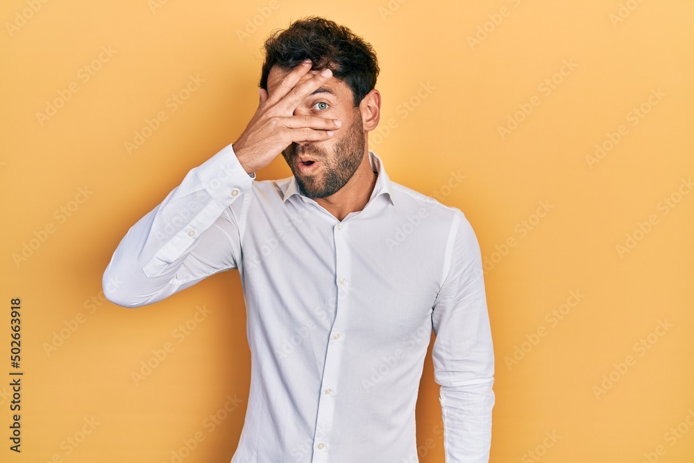 Handsome man with beard wearing casual white t shirt peeking in shock covering face and eyes with hand, looking through fingers afraid Handsome man with beard wearing casual white t shirt peeking in shock covering face and eyes with hand, looking through fingers afraid