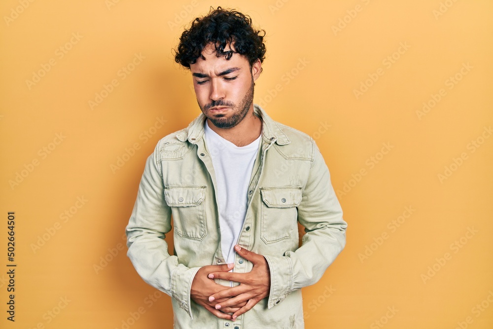 Young hispanic man wearing casual clothes with hand on stomach because indigestion, painful illness feeling unwell. ache concept. Young hispanic man wearing casual clothes with hand on stomach because indigestion, painful illness feeling unwell. ache concept.