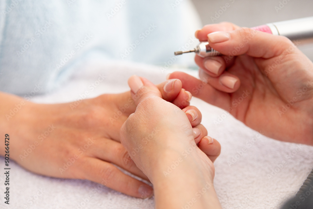 Manicure process in beauty salon, cleaning of nails by a milling cutter. Manicurist filing client's nails at table. Removing the nail plate with a milling machine. nail care concept Manicure process in beauty salon, cleaning of nails by a milling cutter. Manicurist filing client's nails at table. Removing the nail plate with a milling machine. nail care concept