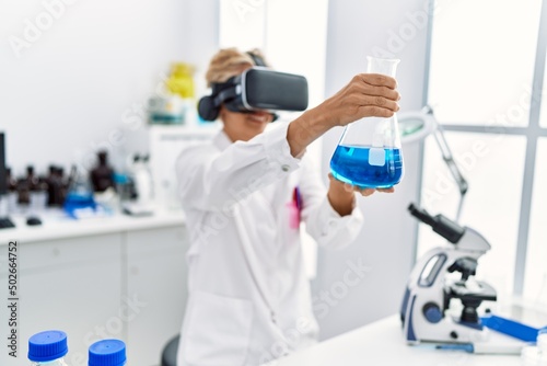 Middle age blonde woman wearing scientist uniform using vr goggles working at laboratory