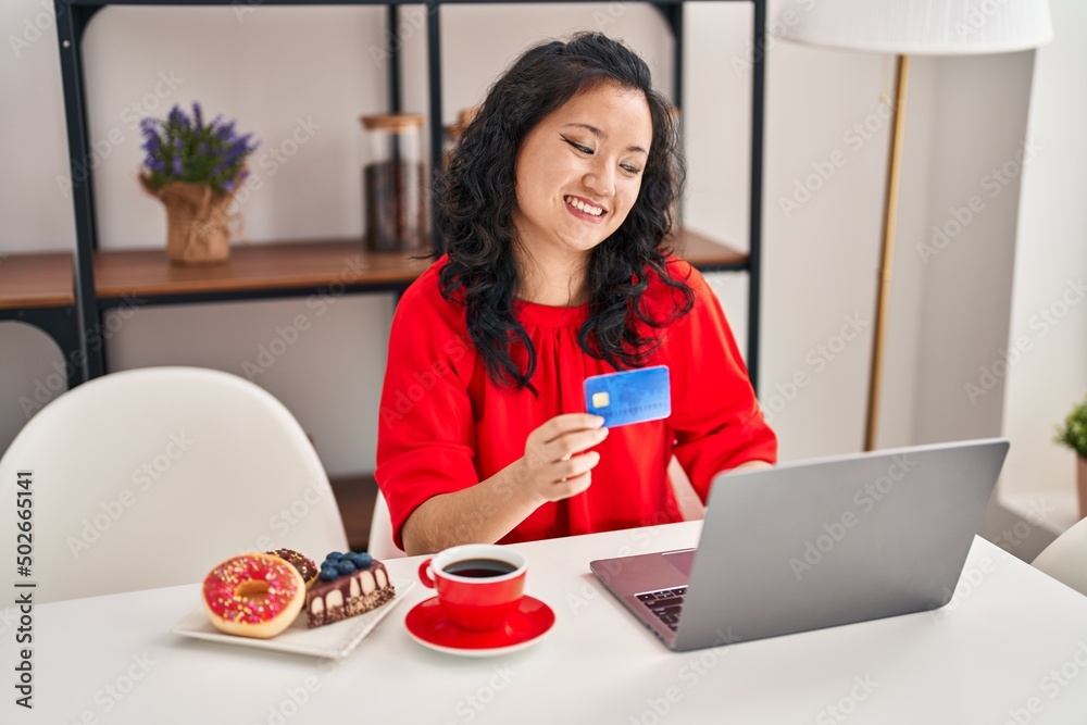 Young chinese woman having breakfast using laptop and credit card at home