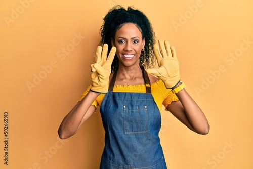Middle age african american woman wearing professional apron showing and pointing up with fingers number eight while smiling confident and happy.