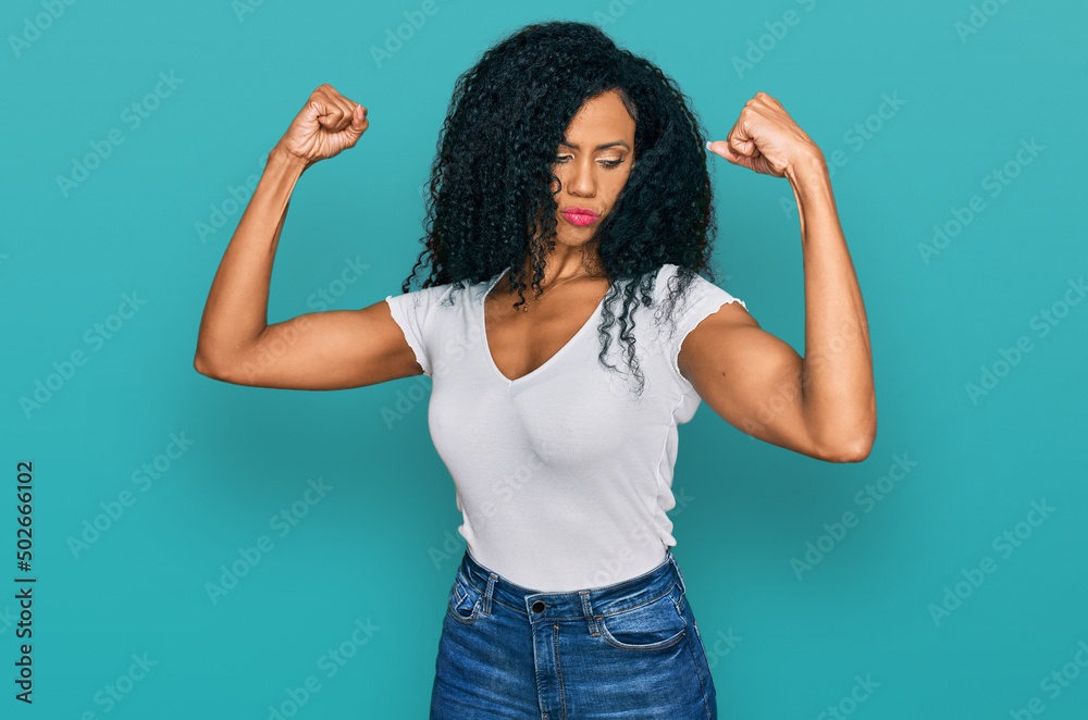 Middle age african american woman wearing casual white t shirt showing arms muscles smiling proud. fitness concept. Middle age african american woman wearing casual white t shirt showing arms muscles smiling proud. fitness concept.