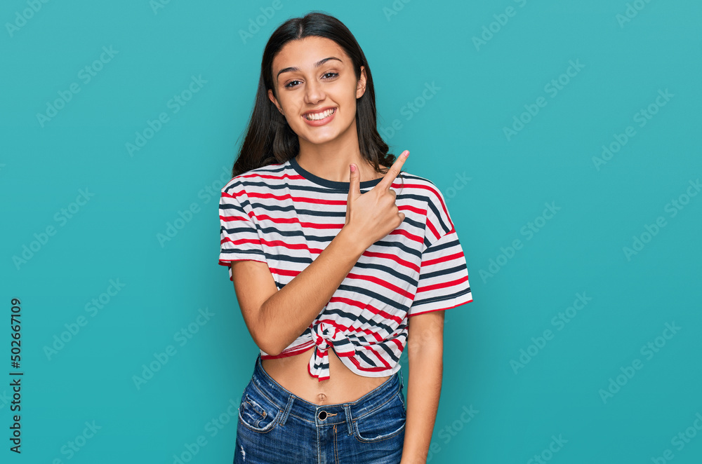 Young hispanic girl wearing casual clothes cheerful with a smile of face pointing with hand and finger up to the side with happy and natural expression on face Young hispanic girl wearing casual clothes cheerful with a smile of face pointing with hand and finger up to the side with happy and natural expression on face