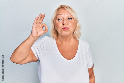 Middle age blonde woman doing ok positive gesture puffing cheeks with funny face. mouth inflated with air, catching air.