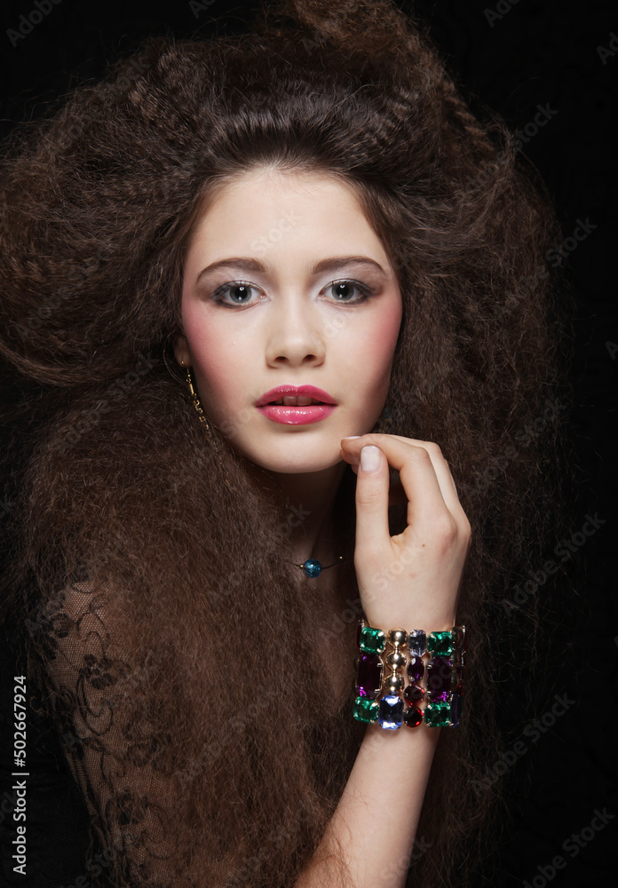 Obraz premium Beautiful young woman with long curly hair and evening make-up wearing black dress and jewerly