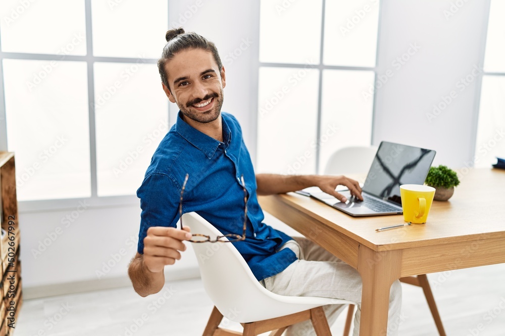 Obraz premium Handsome hispanic man working with laptop wearing glasses at the office