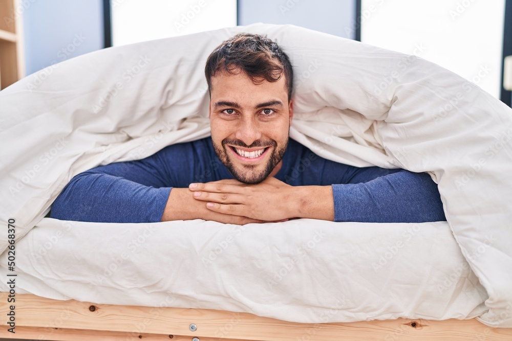 Young hispanic man smiling confident lying on bed at bedroom