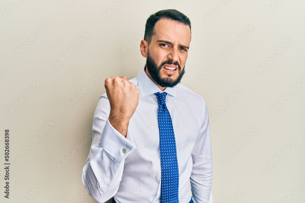 Young man with beard wearing business tie angry and mad raising fist frustrated and furious while shouting with anger. rage and aggressive concept. Young man with beard wearing business tie angry and mad raising fist frustrated and furious while shouting with anger. rage and aggressive concept.