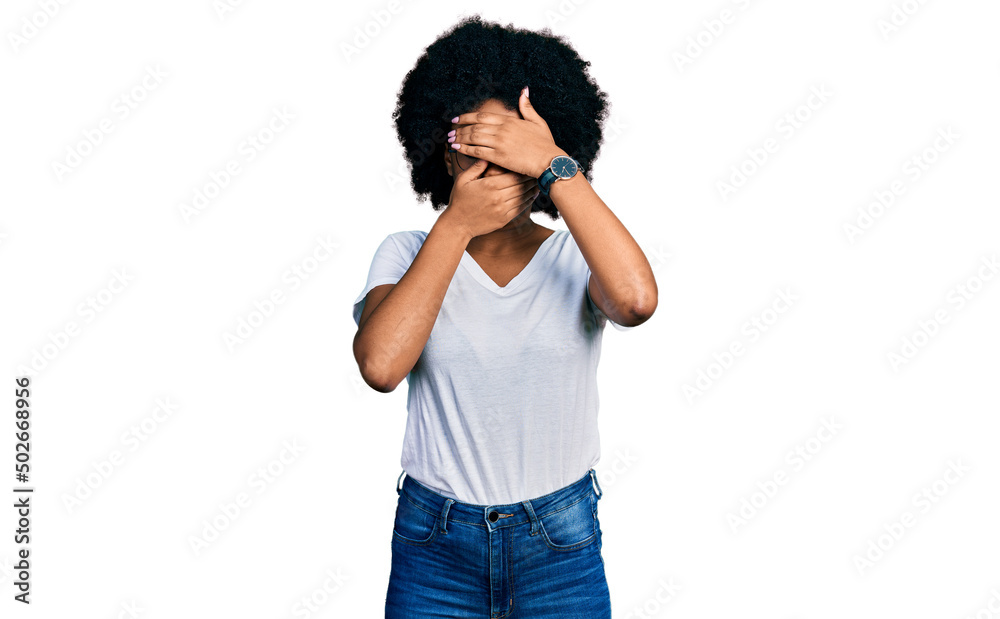 Young african american woman wearing casual white t shirt covering eyes and mouth with hands, surprised and shocked. hiding emotion Young african american woman wearing casual white t shirt covering eyes and mouth with hands, surprised and shocked. hiding emotion
