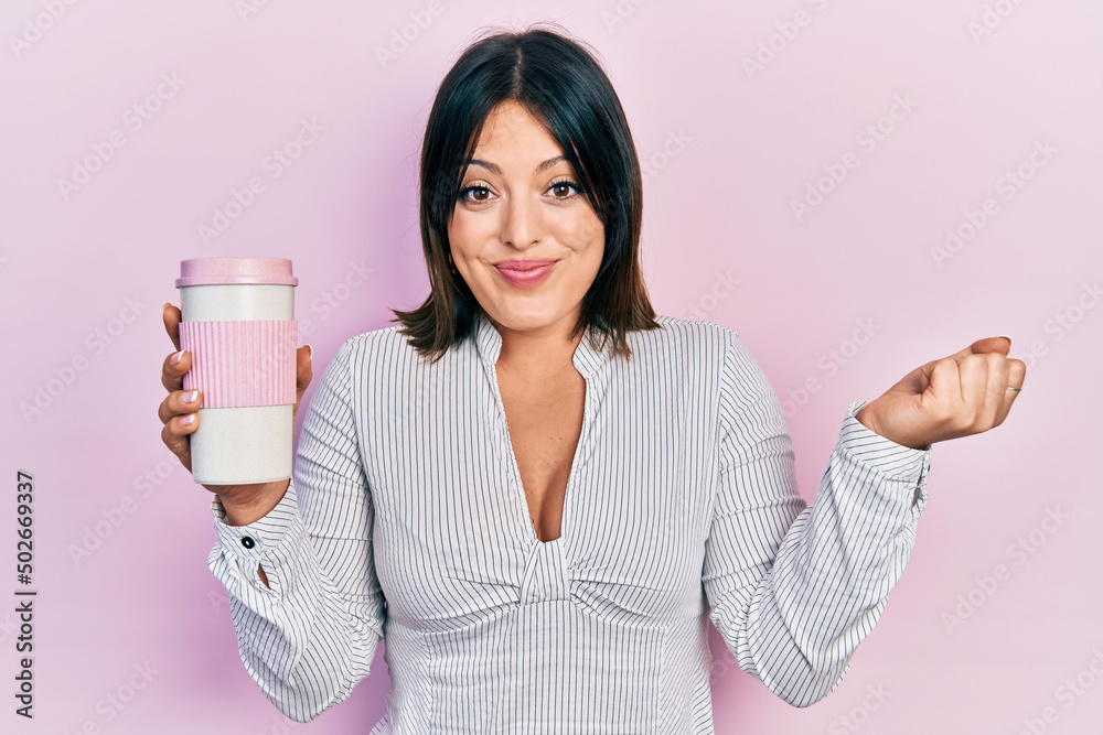 Young hispanic woman drinking a cup of coffee screaming proud, celebrating victory and success very excited with raised arm
