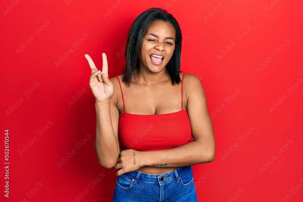 Young african american girl wearing casual style with sleeveless shirt smiling with happy face winking at the camera doing victory sign. number two. Young african american girl wearing casual style with sleeveless shirt smiling with happy face winking at the camera doing victory sign. number two.