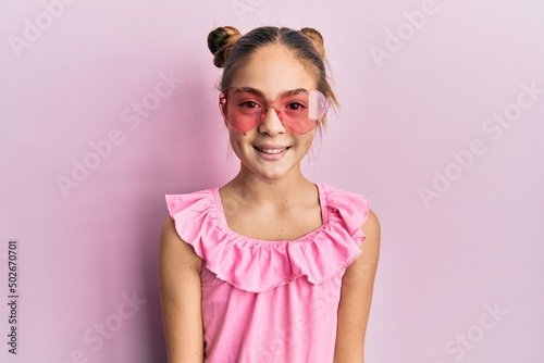 Beautiful brunette little girl wearing heart shaped sunglasses with a happy and cool smile on face. lucky person.