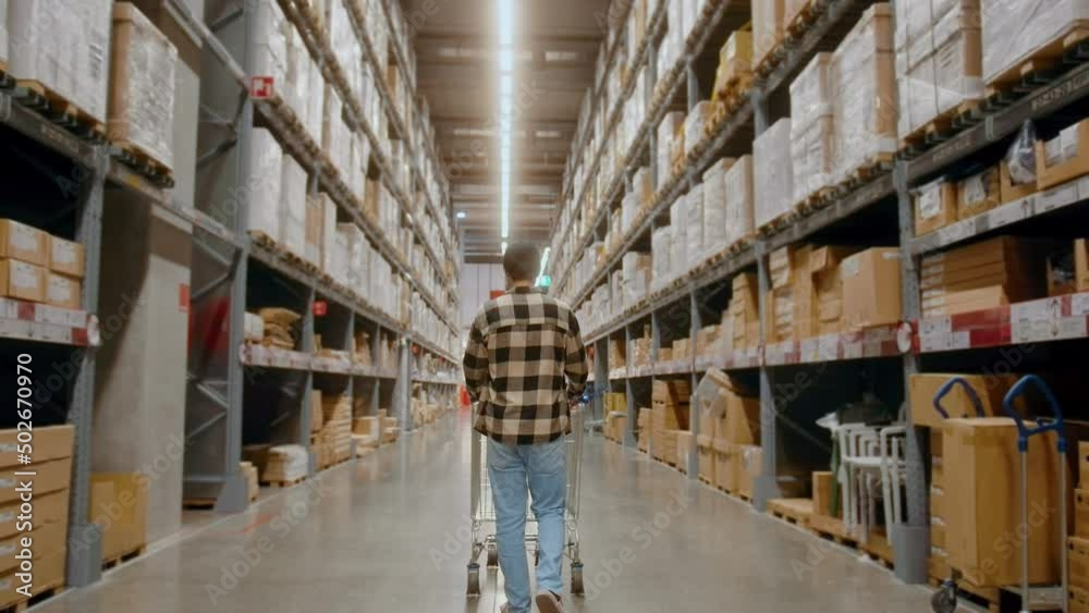 A young Interior designer man pushing supermarket cart looking for home decoration accessories in warehouse A young Interior designer man pushing supermarket cart looking for home decoration accessories in warehouse