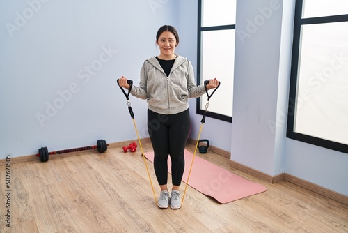 Young hispanic woman smiling confident training using elastic band at sport center