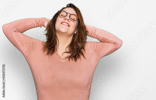 Young plus size woman wearing casual clothes and glasses relaxing and stretching, arms and hands behind head and neck smiling happy