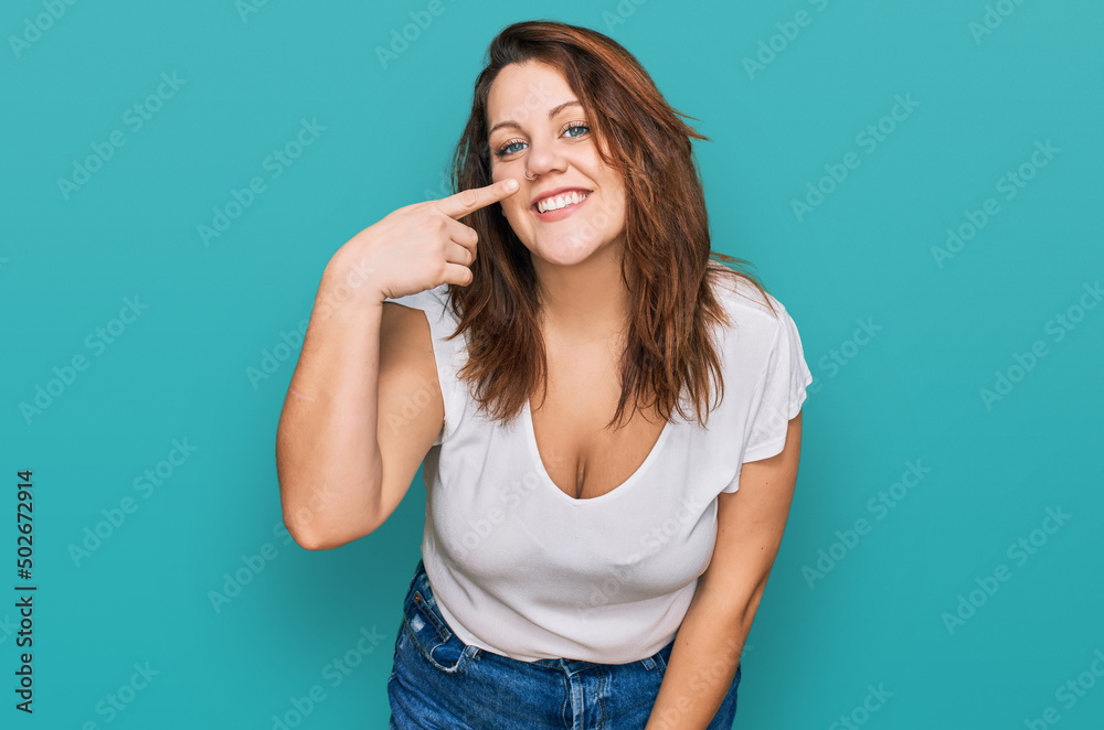 Young plus size woman wearing casual white t shirt pointing with hand finger to face and nose, smiling cheerful. beauty concept
