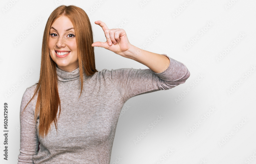Young irish woman wearing casual clothes smiling and confident gesturing with hand doing small size sign with fingers looking and the camera. measure concept. Young irish woman wearing casual clothes smiling and confident gesturing with hand doing small size sign with fingers looking and the camera. measure concept.