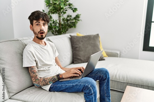 Hispanic man with beard sitting on the sofa afraid and shocked with surprise expression, fear and excited face.