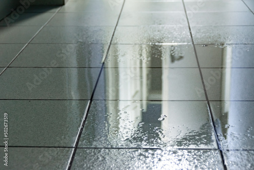 a large puddle on the tiled floor was caused by water from the ceiling as a result of a roof leak or a burst water pipe