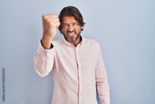 Handsome middle age man wearing elegant shirt background angry and mad raising fist frustrated and furious while shouting with anger. rage and aggressive concept.