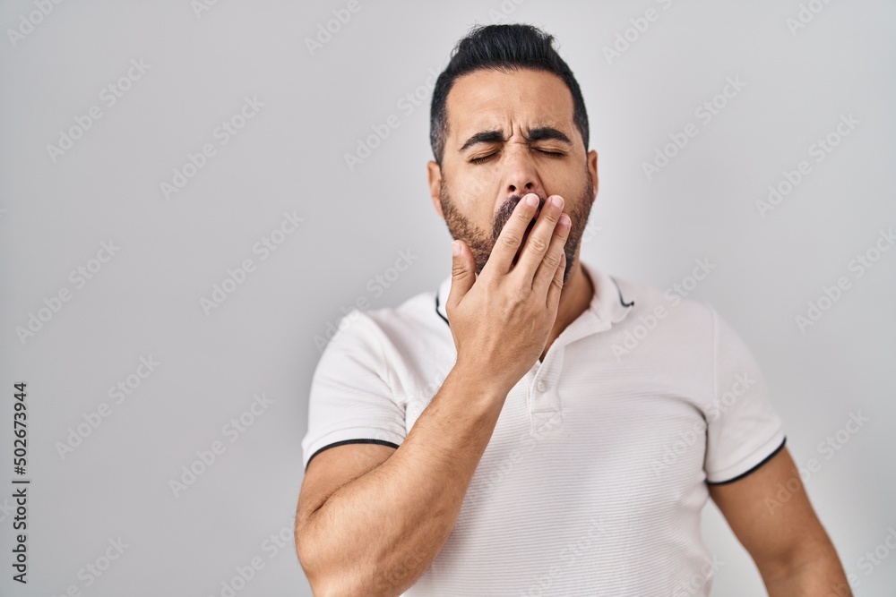 Young hispanic man with beard wearing casual clothes over white background bored yawning tired covering mouth with hand. restless and sleepiness. Young hispanic man with beard wearing casual clothes over white background bored yawning tired covering mouth with hand. restless and sleepiness.
