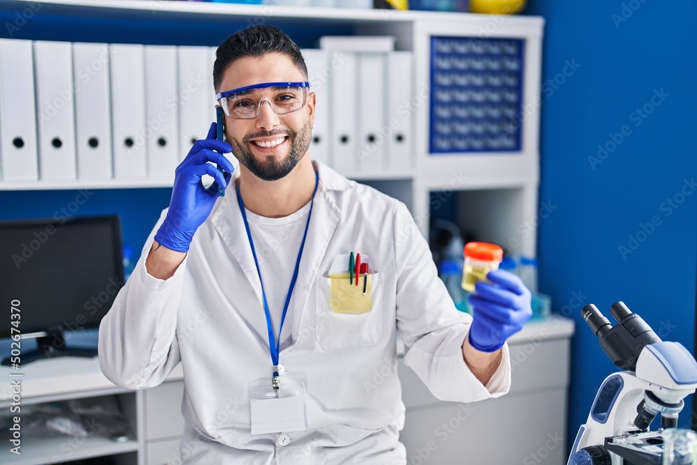 Young arab man scientist talking on the smartphone holding urine test tube analysis at laboratory Young arab man scientist talking on the smartphone holding urine test tube analysis at laboratory