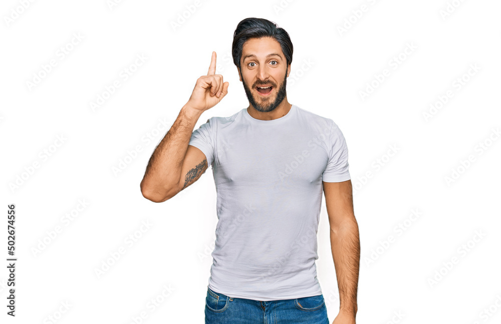 Young hispanic man wearing casual white t shirt pointing finger up with successful idea. exited and happy. number one.