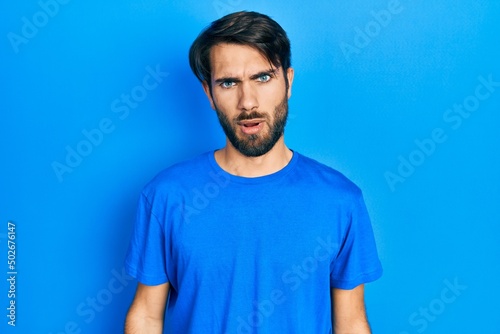Young hispanic man wearing casual clothes in shock face, looking skeptical and sarcastic, surprised with open mouth