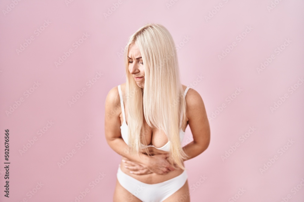 Obraz premium Caucasian woman wearing lingerie over pink background with hand on stomach because nausea, painful disease feeling unwell. ache concept.