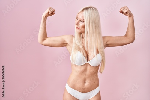 Caucasian woman wearing lingerie over pink background showing arms muscles smiling proud. fitness concept.