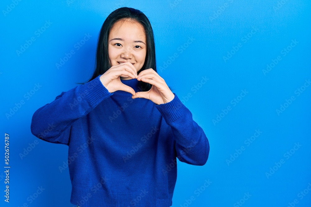 Young chinese girl wearing casual clothes smiling in love doing heart symbol shape with hands. romantic concept. Young chinese girl wearing casual clothes smiling in love doing heart symbol shape with hands. romantic concept.