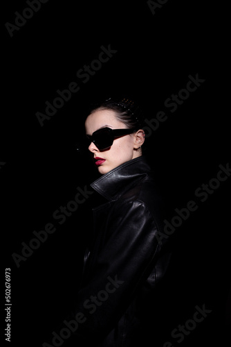 woman in leather coat and black sunglasses, black background