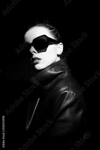 woman in leather coat and sunglasses, black background