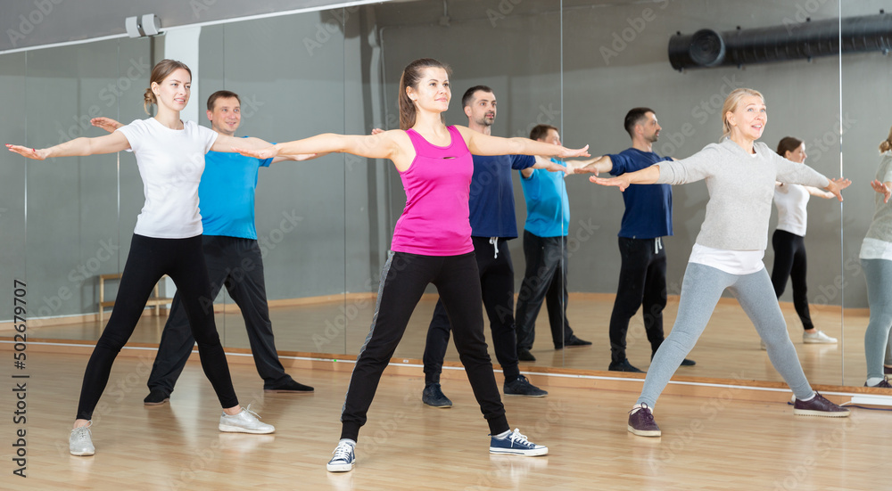 Adult females and males doing stretching workout before group dance training