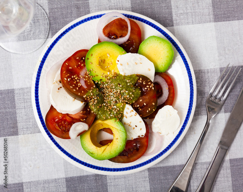 Portion of traditional Italian salad, caprese, made of sliced tomatoes, mozrella, onion and avocado. photo