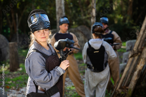 Young woman wearing uniform and holding gun ready for playing with friends on paintball outdoor