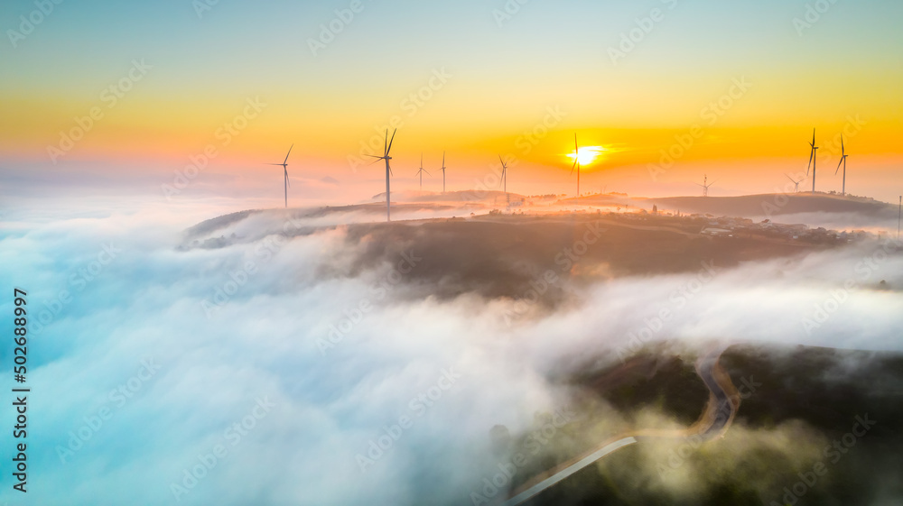 Aerial view top hill at dawn with fog covering small village in valley, beautiful wind power poles rising high to welcome a peaceful new day in highlands Da Lat, Vietnam