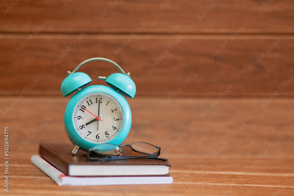 Colorful alarm clock, books, glasses on wooden table on wood grain background. back to school concept Colorful alarm clock, books, glasses on wooden table on wood grain background. back to school concept