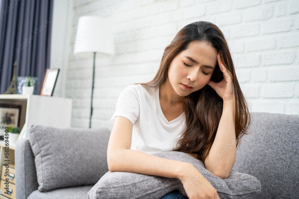 Beautiful Asian woman wearing white T-shirt feeling stress and headache on sofa. She used her hand to touch her face. Office syndrome concept. Beautiful Asian woman wearing white T-shirt feeling stress and headache on sofa. She used her hand to touch her face. Office syndrome concept.